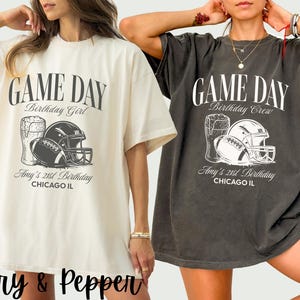 Op de afbeelding: Twee oversized T-shirts, &eacute;&eacute;n ivoorkleurig en &eacute;&eacute;n donkergrijs, met een voetbalthema. Het ontwerp bevat een voetbal, helm en bierpul, met de tekst "GAME DAY" en "Amy's 21st Birthday, Chicago IL."