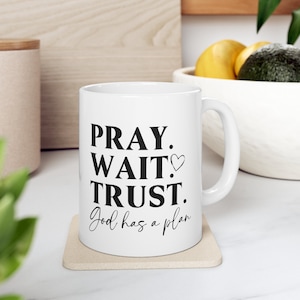 May include: White ceramic mug with black text that reads "Pray. Wait. Trust. God has a plan".