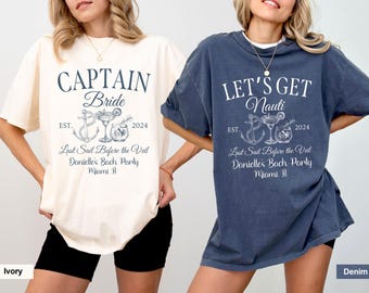 May include: Two oversized t-shirts with a nautical theme. The ivory t-shirt says "Captain Bride" and the denim t-shirt says "Let's Get Nauti". Both shirts have a graphic of an anchor, a cocktail glass, and a bottle. The text "Last Sail Before the Veil" and "Danielle's Bach Party" are also on the shirts.