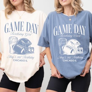 Op de afbeelding: Twee oversized T-shirts, &eacute;&eacute;n ivoor en &eacute;&eacute;n jeansblauw, met een voetbalthema. Het ontwerp bevat een voetbal, helm en bierpul, met de tekst "GAME DAY" en "Amy's 21st Birthday, Chicago IL."