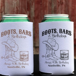 K&ouml;nnte beinhalten: Zwei wei&szlig;e Getr&auml;nkedosenk&uuml;hler mit einem schwarzen und braunen Design. Das Design zeigt ein Paar Cowboystiefel, einen Cowboyhut und ein Glas Whisky. Der Text auf den K&uuml;hlern lautet "Boots, Bars & Birthdays" und "Amy's 40th Birthday Nashville, TN".