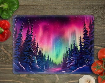 May include: Rectangular glass cutting board featuring a vibrant illustration of the Aurora Borealis. The artwork depicts a colorful night sky with shades of pink, purple, and green, and a forest of dark blue trees.