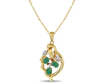 Puede incluir: Collar dorado con un colgante que presenta tres esmeraldas ovaladas y pequeños acentos de diamantes. El colgante tiene un diseño fluido. La cadena es delicada y dorada.