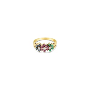 May include: A gold ring featuring a cluster of small, round-cut gemstones arranged in a horizontal row. The stones include blue sapphires on the left, red rubies in the center, and green emeralds on the right, interspersed with three small, clear diamonds.