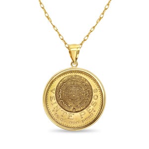 May include: A gold-colored pendant necklace featuring a large, round coin-like charm. The charm has an intricate design in the center, surrounded by text. The chain and pendant are a bright, shiny gold color. The pendant appears to be a Mexican 20 Pesos coin.