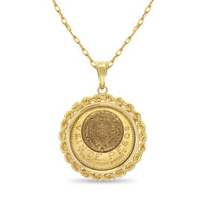 May include: A gold-toned pendant necklace featuring a round coin design. The coin has intricate detailing and is encircled by a twisted rope-like border. The necklace chain is also gold-toned, with a delicate link pattern.