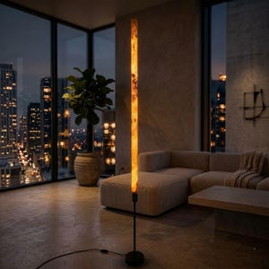 Peut inclure: Un lampadaire haut et élancé doté d'un abat-jour cylindrique vertical de couleur ambre lumineuse avec une texture marbrée. Le luminaire est soutenu par une fine tige en métal noir et une base circulaire noire, reliée par un cordon d'alimentation noir.