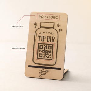 May include: A rectangular light-colored wooden sign with a stand, featuring a laser-engraved jar graphic, the text "VIRTUAL TIP JAR", a central QR code placeholder, a "YOUR LOGO" section at the top, and the words "Thank you!" at the bottom.