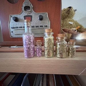 Könnte beinhalten: Ein Set aus drei Keramikbechern mit gesprenkelter, matter Oberfläche. Die Becher sind in Creme-, Hellbraun- und Dunkelbrauntönen gehalten. Jeder Becher hat ein schlichtes, minimalistisches Design.