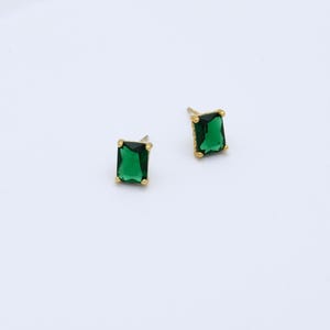 May include: A pair of gold earrings with emerald green square-shaped stones.