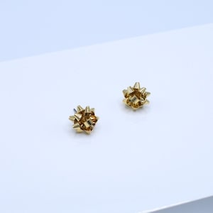 May include: A pair of gold bow-shaped stud earrings.