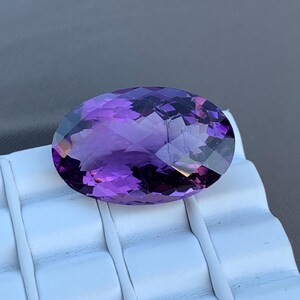 K&ouml;nnte beinhalten: Ein gro&szlig;er, ovaler Amethyst-Edelstein mit tiefem Lilafarbton. Der Edelstein ist facettiert und hat einen hohen Glanz.