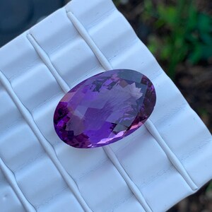 K&ouml;nnte beinhalten: Ein gro&szlig;er, ovaler Amethyst-Edelstein mit tiefem Lilafarbton. Der Edelstein ist facettiert und hat eine hohe Klarheit.