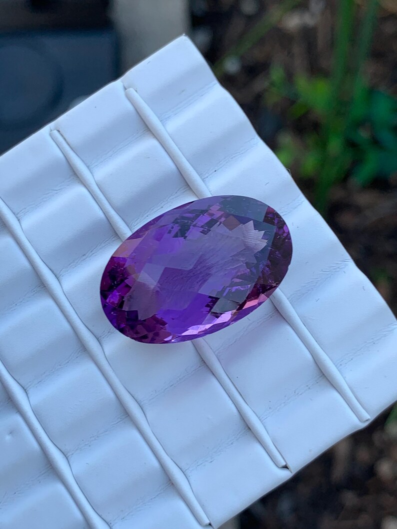 K&ouml;nnte beinhalten: Ein gro&szlig;er, ovaler Amethyst-Edelstein mit tiefem Lilafarbton. Der Edelstein ist facettiert und hat eine hohe Klarheit.