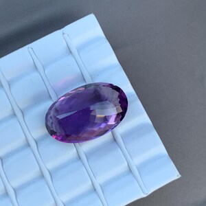 K&ouml;nnte beinhalten: Ein gro&szlig;er, ovaler Amethyst-Edelstein mit tiefem Lilafarbton. Der Edelstein ist facettiert und hat einen hohen Glanzgrad.