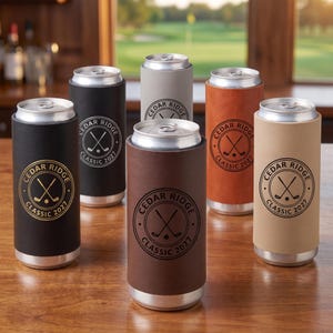 May include: Six slim beverage can coolers in black, grey, brown, orange, and tan colors. Each cooler features a circular logo with the text Cedar Ridge Classic 2027 and an illustration of two crossed golf clubs and a golf ball in the center.