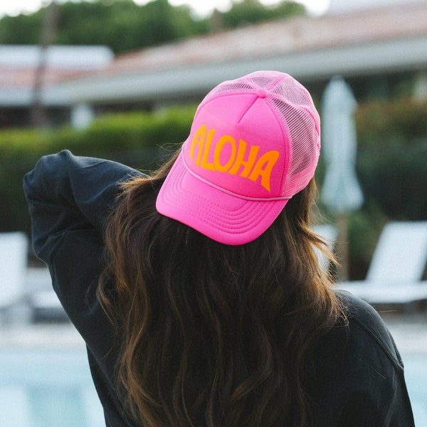 May include: A pink trucker hat with a mesh back and an orange "ALOHA" graphic.