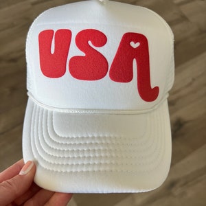 May include: White trucker hat with a red "USA" logo and a small white heart in the "A".