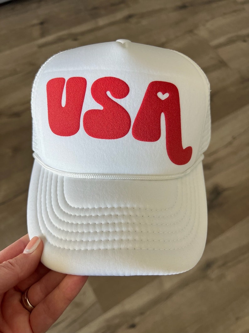 May include: White trucker hat with a red "USA" logo and a small white heart in the "A".
