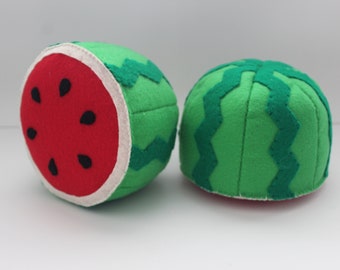 May include: Two felt watermelon toys. One watermelon is cut in half, revealing a red interior with black seeds. The other watermelon is whole, with a green exterior and a zig-zag pattern.