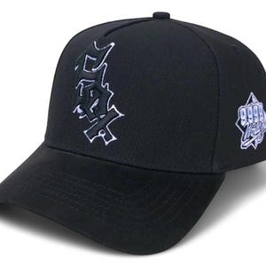 Puede incluir: Gorra de béisbol negra con visera curva. La gorra presenta texto bordado blanco en la parte delantera y un logotipo blanco en el lateral. El texto frontal está estilizado. El logotipo lateral incluye el texto "9999" y "Hustle".
