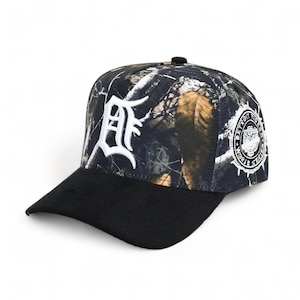 Puede incluir: Una gorra de béisbol negra y de camuflaje con una "D" bordada en blanco en la parte delantera y un parche blanco de "Detroit Tigers World Series" en el lateral.
