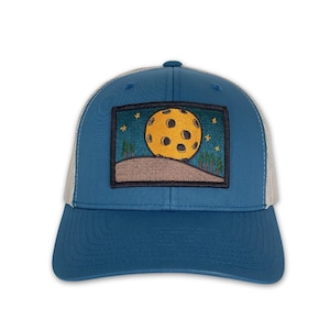 May include: A blue and gray trucker hat with a patch featuring a yellow moon with craters and stars in the night sky.