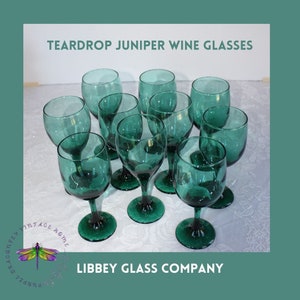 May include: Ten teal green teardrop-shaped wine glasses with a textured surface. The glasses are arranged in a circle on a white surface. The text "TEARDROP JUNIPER WINE GLASSES" is at the top of the image. The text "LIBBEY GLASS COMPANY" is at the bottom of the image.