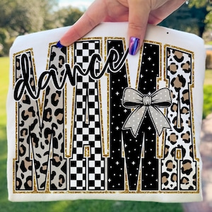 May include: White t-shirt with the words "Dance Mama" in a mix of leopard print, checkered, and star patterns. The word "dance" is in a cursive font, and a gray bow is featured on the right side.