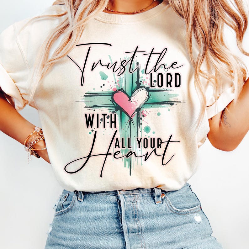May include: A cream colored t-shirt with a green and white cross and a pink heart. The text on the shirt reads "Trust the Lord with all your heart".