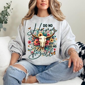 Może przedstawiać: Jasnoszara bluza z nadrukiem czaszki byka z kwiatowymi akcentami i napisem "Do No Harm But Take No Bull". Projekt zawiera motyle i mieszankę kolorowych kwiat&oacute;w.