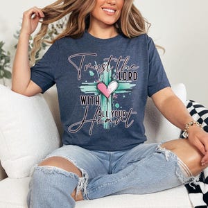 May include: A navy blue t-shirt with a graphic of a cross and a heart. The text on the shirt reads "Trust the Lord with all your heart".