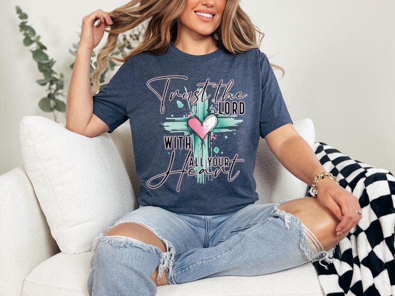 May include: A navy blue t-shirt with a graphic of a cross and a heart. The text on the shirt reads "Trust the Lord with all your heart".