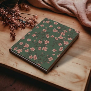 May include: A green journal with a floral pattern featuring pink flowers on a wooden surface.