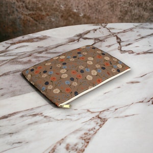 May include: A brown zippered pouch with a floral pattern featuring white, blue, and orange flowers on a brown background. The pouch is lying on a marble surface.