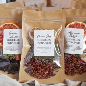 May include: Several brown paper pouches filled with simmering potpourri ingredients. Each pouch has a label with a different name: "Summer Market," "Flower Shop," and "Afternoon Delight." The pouches contain dried fruit slices, herbs, and spices.