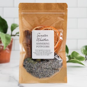 May include: A brown kraft paper pouch containing simmering potpourri with dried orange slices, cinnamon sticks, and lavender. The white label reads Sweater Weather SIMMERING POTPOURRI and includes instructions to add 2-3 cups of water.