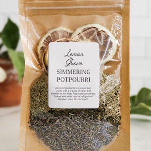 May include: A brown kraft paper pouch containing simmering potpourri with dried lemon slices, lavender buds, and herbs. The white label reads Lemon Grove SIMMERING POTPOURRI with instructions to add 2-3 cups of water and simmer on low heat. Do not ingest.