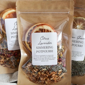 May include: Clear cellophane pouches filled with dried botanicals and citrus slices. Each pouch has a label with the text "Citrus Lavender Simmering Potpourri". The pouches are sealed and packaged in brown paper.