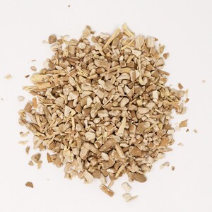 May include: A pile of dried, light brown, irregularly shaped root pieces. The fragments vary in size and texture, displaying a woody, fibrous appearance with a mix of small chunks and thin, splinter-like slivers scattered across the surface.