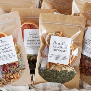 May include: Several clear pouches filled with simmering potpourri, each with a different blend of dried herbs, spices, and citrus slices. Each pouch has a label with a unique name like "Citrus Lavender" or "Afternoon Delight".