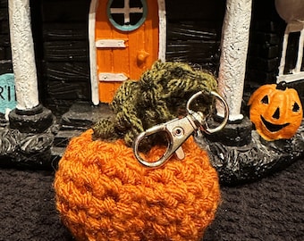 May include: An orange crocheted pumpkin with green leaves and a silver-colored clasp. The pumpkin is a handmade item, perfect for Halloween or fall decor. The pumpkin is approximately 3 inches in diameter.