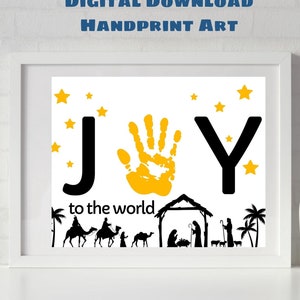 May include: Framed art print with the word "JOY" in black, featuring a yellow handprint in place of the "O". The print includes the text "to the world" and a silhouette of a nativity scene with stars.