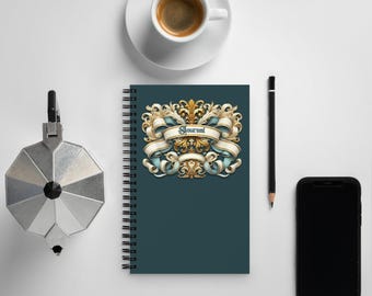 May include: A dark teal spiral bound journal with a gold and white ornate design featuring the word "Journal" on a banner.