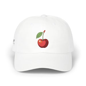 May include: White baseball cap featuring a detailed illustration of a red cherry with a green leaf. The cherry design is centered on the front of the cap. The cap has a curved brim and a classic six-panel design.