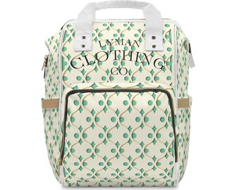 May include: A cream-colored backpack with a repeating pattern of teal circles and gold diamond shapes. The bag has a top handle, two side pockets, and the text "LYMAN CLOTHING CO." on the front.