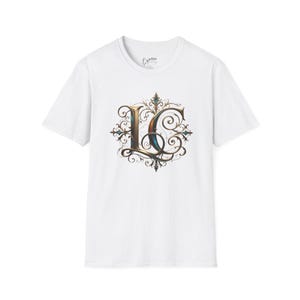 May include: White t-shirt featuring a decorative letter "L" in an ornate, vintage style. The design incorporates gold, teal, and brown hues with intricate scrollwork and flourishes. The shirt has a classic crew neck and short sleeves.