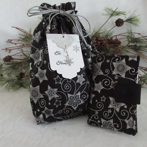 May include: A black fabric gift bag with a silver star and swirl pattern. The bag has a drawstring closure and a white gift tag that says "To" and "From".