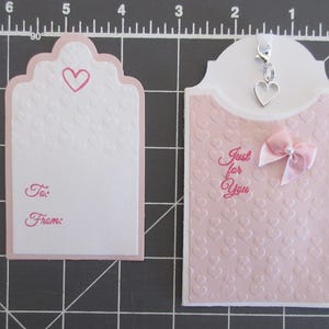 May include: Two pink gift tags with a heart design. One tag has the words "Just for You" and a pink bow. The other tag has the words "To:" and "From:".