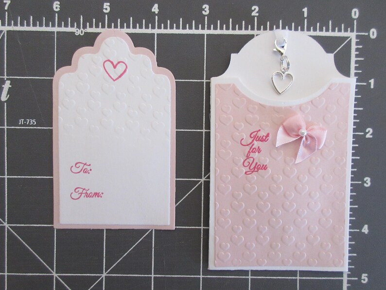 May include: Two pink gift tags with a heart design. One tag has the words "Just for You" and a pink bow. The other tag has the words "To:" and "From:".